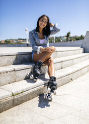 Spain, Gijon, smiling teenage girl with roller skates sitting on stairs - MGOF000999