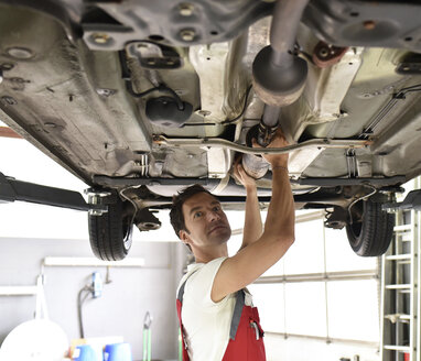 Automechaniker bei der Arbeit in einer Reparaturwerkstatt, der den Unterboden eines Autos überprüft - LYF000496