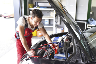 Automechaniker bei der Arbeit in einer Reparaturwerkstatt, Aufladen einer Autobatterie - LYF000528