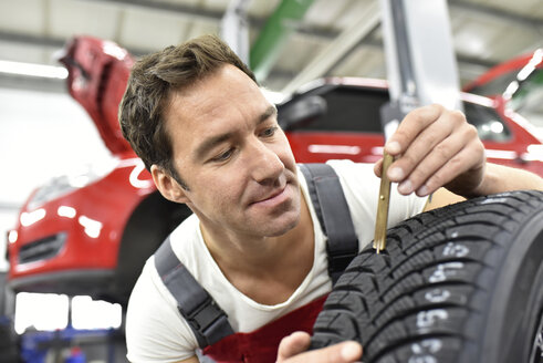 Automechaniker bei der Arbeit in einer Reparaturwerkstatt, Kontrolle der Mustertiefe - LYF000522