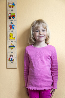 Portrait of smiling little girl standing beside a yardstick - JFEF000696