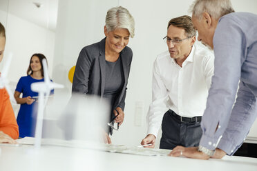 Geschäftsleute besprechen einen Plan mit einem Windradmodell auf einem Konferenztisch - MFF002143