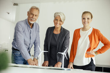 Three smiling business people with wind turbine model on conference table - MFF002144