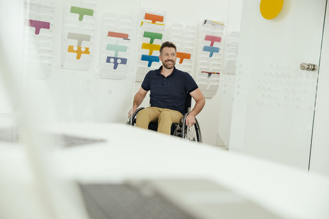 Lächelnder Mann im Rollstuhl in einem modernen Büro, lizenzfreies Stockfoto