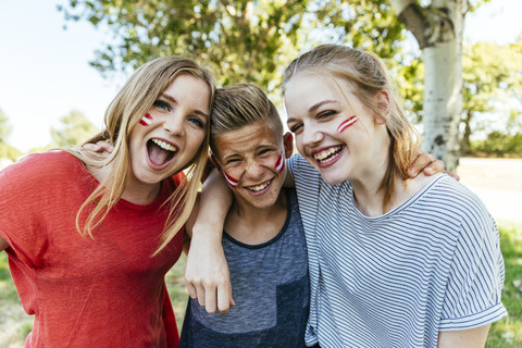 Österreich, drei Teenager mit aufgemalten Nationalfarben auf den Wangen, die gemeinsam feiern, lizenzfreies Stockfoto