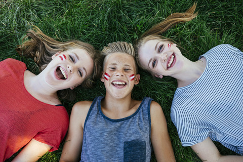 Österreich, drei Jugendliche mit aufgemalten Nationalfarben auf den Wangen liegen auf einer Wiese, lizenzfreies Stockfoto