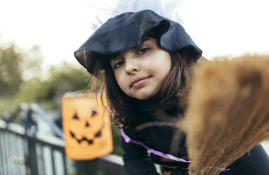Porträt eines als Hexe verkleideten kleinen Mädchens mit Halloween-Laterne und Besen - MGOF000673