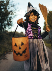 Porträt eines als Hexe verkleideten kleinen Mädchens mit Halloween-Laterne und Besen - MGOF000706
