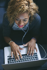 Young woman lying on the couch with earphones using laptop - EBSF000884