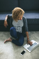 Young woman sitting on the carpet of living room using laptop - EBSF000894