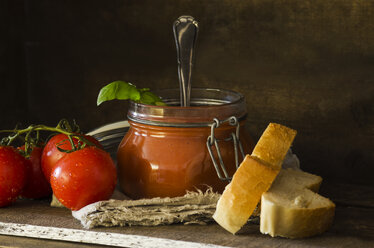 Fresh tomato soup with basil in preserving jar, tomatoes, white bread on wood - ODF001317