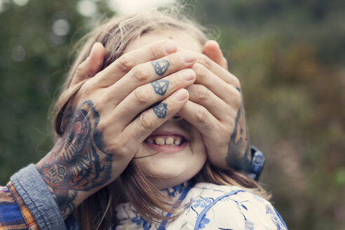 Man's tattooed hands covering eyes of his daughter - XCF000014