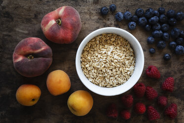 Bowl of oak flakes and different fruits on dark wood - EVG002227