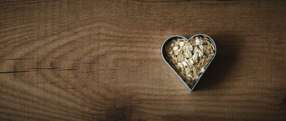 Rolled oats in a heart-shaped cookie cutter on wood - EVGF002239