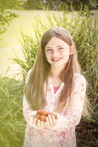 Porträt eines lächelnden Mädchens mit einer Handvoll Erdbeeren, lizenzfreies Stockfoto