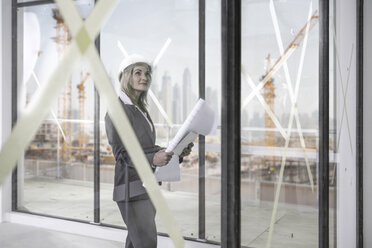 Woman with hard hat and construction plans on construction site - ZEF008362