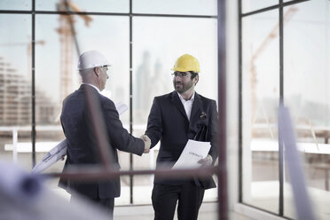 Two businessmen wearing hard hats shaking hands on construction site - ZEF008364