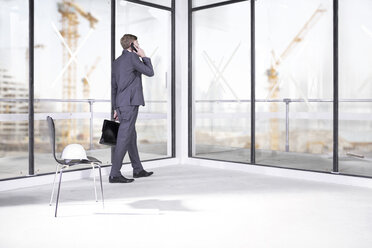 Businessman talking on phone in office under construction - ZEF008374