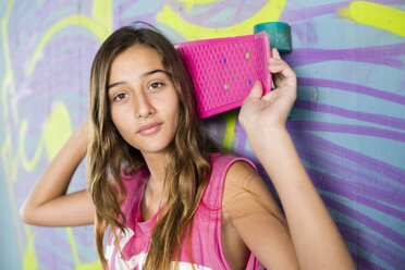 Porträt eines Teenagers, der ein Skateboard vor einer Wand mit Graffiti hält - GEMF000362