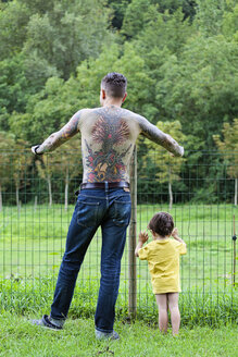 Back view of a tattooed man with his little son standing in front of a fence - XCF000021