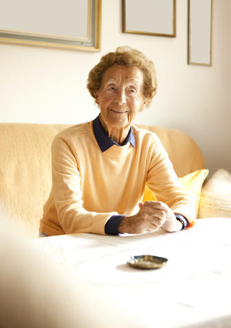Porträt einer älteren Frau auf der Couch in ihrem Wohnzimmer, lizenzfreies Stockfoto