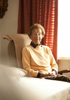 Porträt einer älteren Frau auf einem Sessel in ihrem Wohnzimmer sitzend - MFRF000471