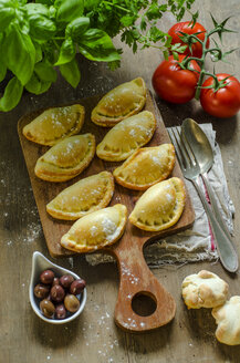 Gefülltes Gebäck mit schwarzen Oliven, Tomaten und Basilikum auf Holzbrett - ODF001322