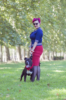 Porträt einer Frau mit gefärbtem Haar, die mit ihrem Pitbull-Terrier auf einer Wiese steht - XCF000023