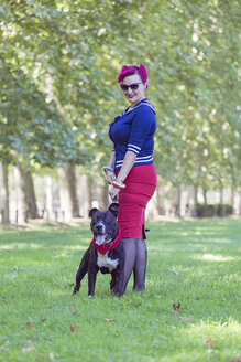 Portrait of woman with dyed hair standing on a meadow with her pit bull terrier - XCF000023