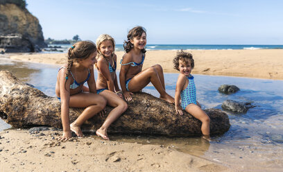 Spanien, Colunga, vier Mädchen sitzen auf Totholz am Strand - MGOF000709