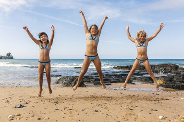 Spain, Colunga, three girls jumping in the air on the beach - MGOF000714