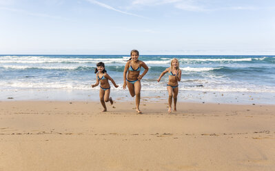 Spain, Colunga, three girls running side by side on the beach - MGOF000719