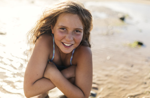 Porträt eines lächelnden Mädchens mit verschränkten Armen am Strand, lizenzfreies Stockfoto