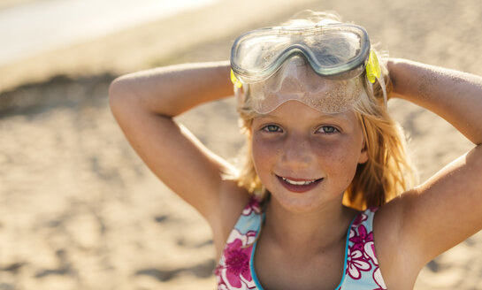 Porträt eines lächelnden blonden kleinen Mädchens mit Tauchermaske und Händen hinter dem Kopf am Strand - MGOF000731