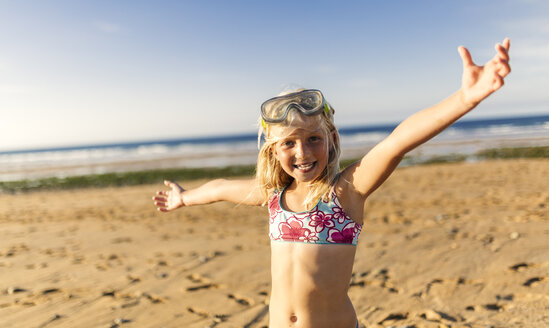 Spanien, Colunga, Porträt eines lächelnden blonden kleinen Mädchens mit Tauchermaske und ausgestreckten Armen am Strand - MGOF000732