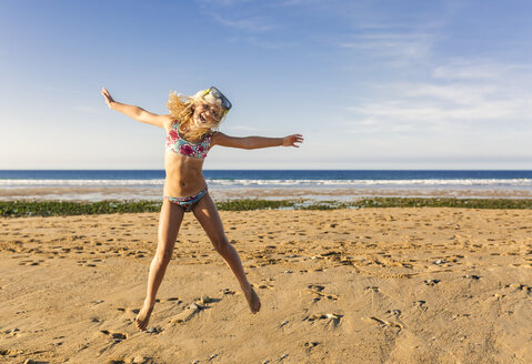Spanien, Colunga, kleines Mädchen mit Tauchermaske, das am Strand in die Luft springt - MGOF000733