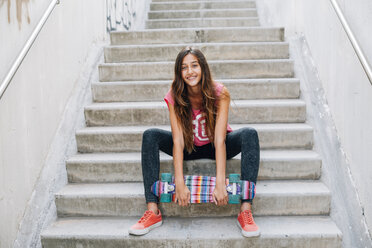 Porträt eines glücklichen Teenager-Mädchens mit buntem Skateboard auf einer Treppe sitzend - GEMF000378