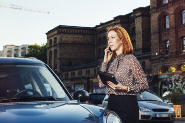 Porträt einer Geschäftsfrau mit Akte, die neben einem geparkten Auto steht und telefoniert - TAM000312