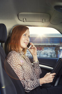Rothaarige Geschäftsfrau sitzt in ihrem Auto und telefoniert mit ihrem Smartphone - TAM000307