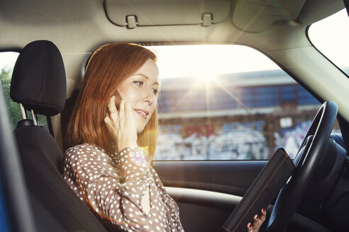 Rothaarige Geschäftsfrau sitzt in ihrem Auto und telefoniert mit ihrem Smartphone - TAM000313