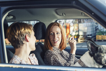 Two female friends sitting in their car talking together - TAM000314