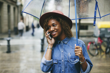 Spanien, Barcelona, Porträt einer lächelnden jungen Frau mit Regenschirm und Smartphone - EBSF000922