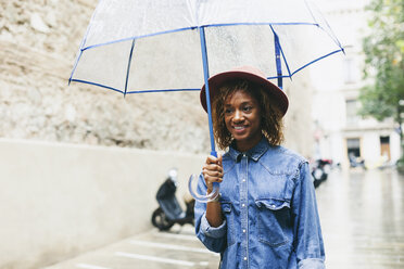 Spanien, Barcelona, Porträt einer lächelnden jungen Frau mit Regenschirm, Hut und Jeanshemd - EBSF000933