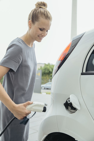 Junge Frau lädt Elektroauto auf, lizenzfreies Stockfoto