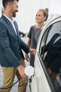 Mann und Frau unterhalten sich beim Aufladen eines Elektroautos - MFF002222