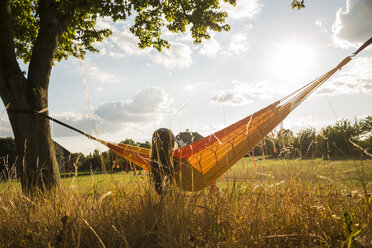 Back view of woman with headphones lying in a hammock relaxing in nature - UUF005634