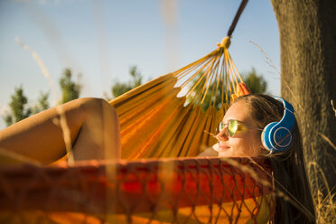Frau mit Sonnenbrille und Kopfhörern entspannt in einer Hängematte - UUF005635
