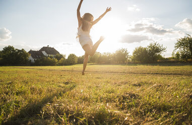 Back view of woman jumping in the air on a meadow at backlight - UUF005639