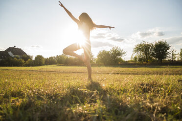 Back view of woman standing on one leg on a meadow at backlight - UUF005640