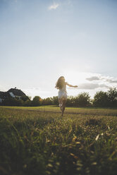 Back view of woman running barefoot on a meadow at backlight - UUF005642